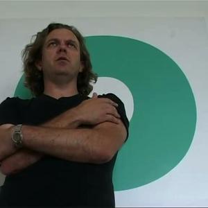 Julian stands with his arms folded looking serious infront of a green circular painting